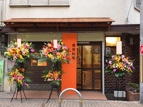 開店当日の店先。祝い花が並ぶ入口(チベママはイラストで表示)